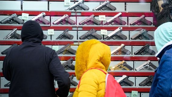 Les gens se tiennent devant l'étalage d'un magasin d'armes qui vend des armes d'alarme et de signalisation. © dpa